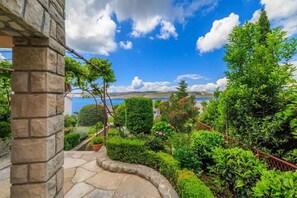 A stone pathway leading to a lush garden with various plants and a view of the sea. - Studio mit Terrasse und Klimaanlage (Jadranovo)