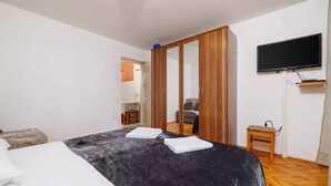 A bedroom with a bed, a wardrobe, a television, and a small table. - Studio mit Terrasse und Klimaanlage (Jadranovo)