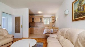 En stue med en beige sofa, et hvidt sofabord og et køkken i baggrunden.