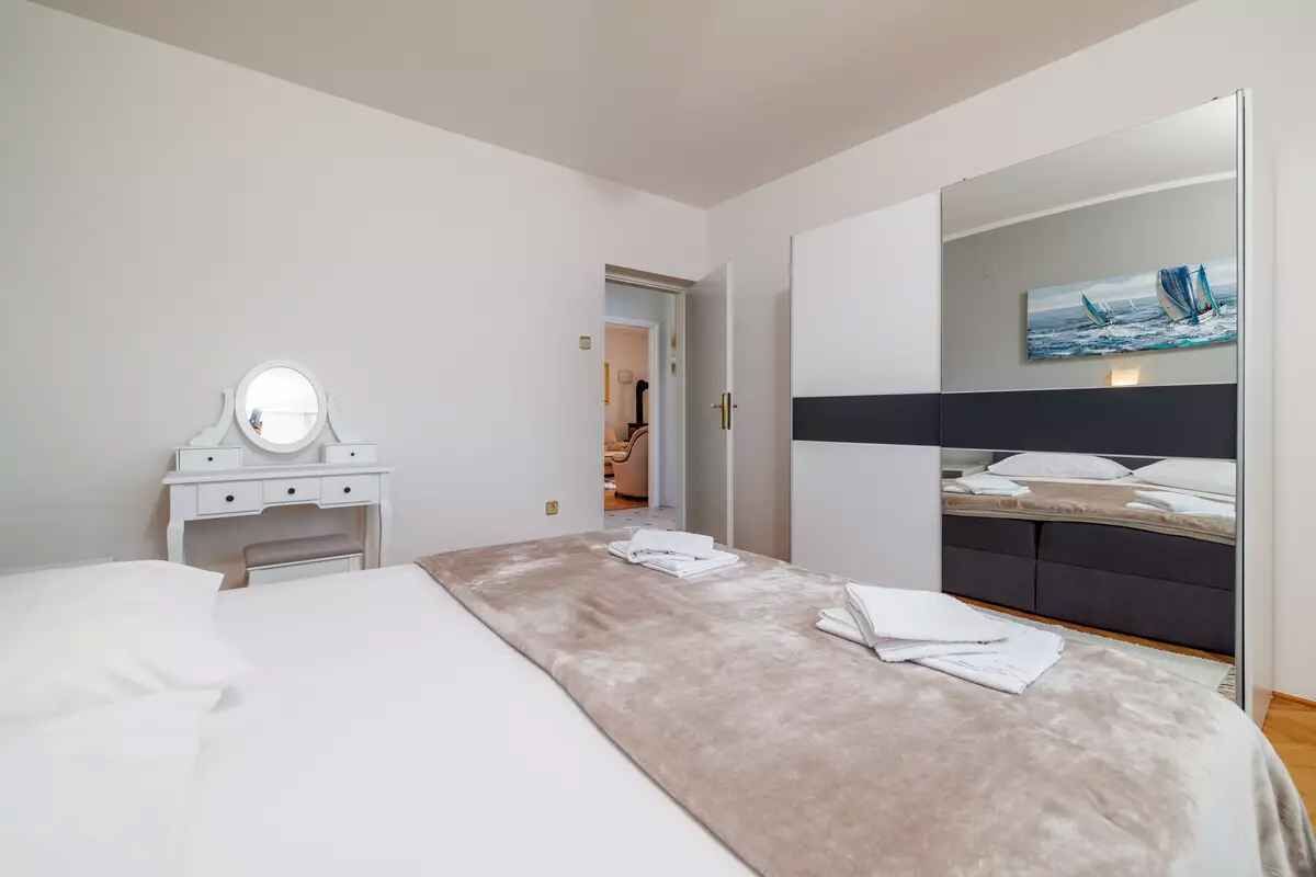 Une chambre d’hôtel moderne dotée d’un grand lit, d’une coiffeuse avec un miroir, d’un tableau au mur et d’un coin salon séparé avec une chaise et une table.