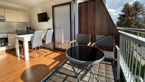 Een moderne keuken met een eethoek, een balkon met uitzicht op bomen en een aan de muur bevestigde televisie.