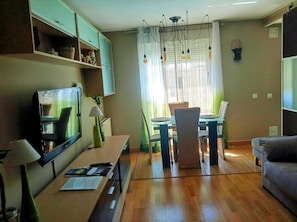 Una sala de estar moderna con comedor, piso de madera, televisor y lámpara de araña.