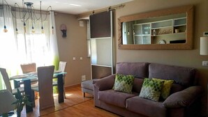 Een woonkamer met een bank, een eettafel met stoelen en een hanglamp.