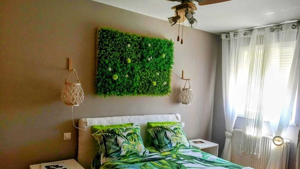 Slaapkamer met een bed, een plafondventilator, een groene wandversiering, een nachtkastje en een raam met gordijnen.