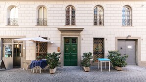 Un bâtiment avec une porte verte, des plantes en pot et une table recouverte d’une nappe bleue.