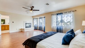 Un dormitorio espacioso con una cama grande, un ventilador de techo y vistas al exterior a través de amplias ventanas.