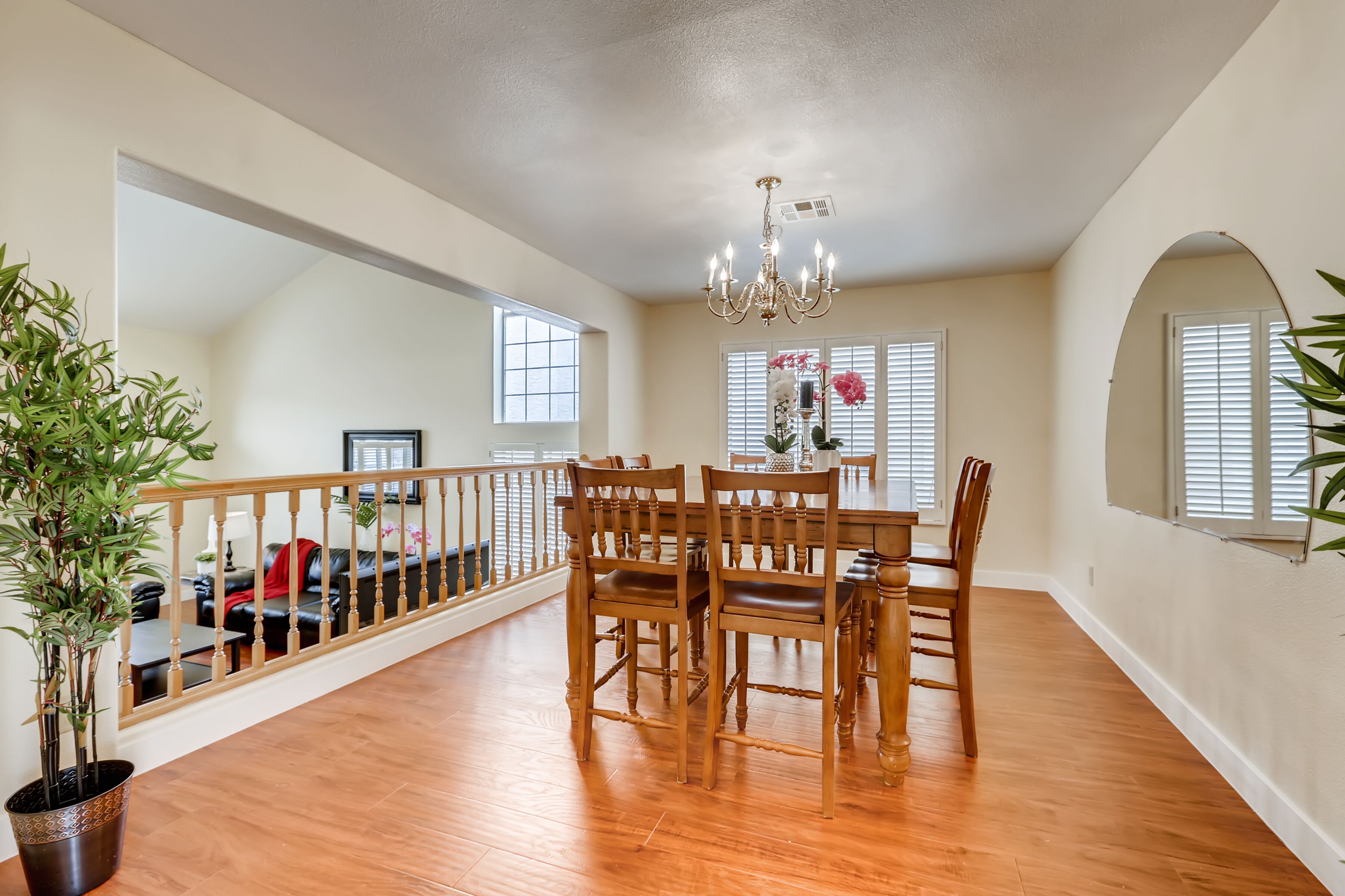 A spacious dining area with a wooden table and chairs, a chandelier, and a potted plant.