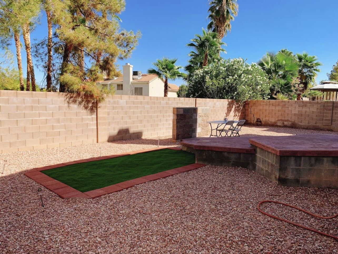 A backyard with a small artificial turf area, a brick wall, and a patio with outdoor furniture.