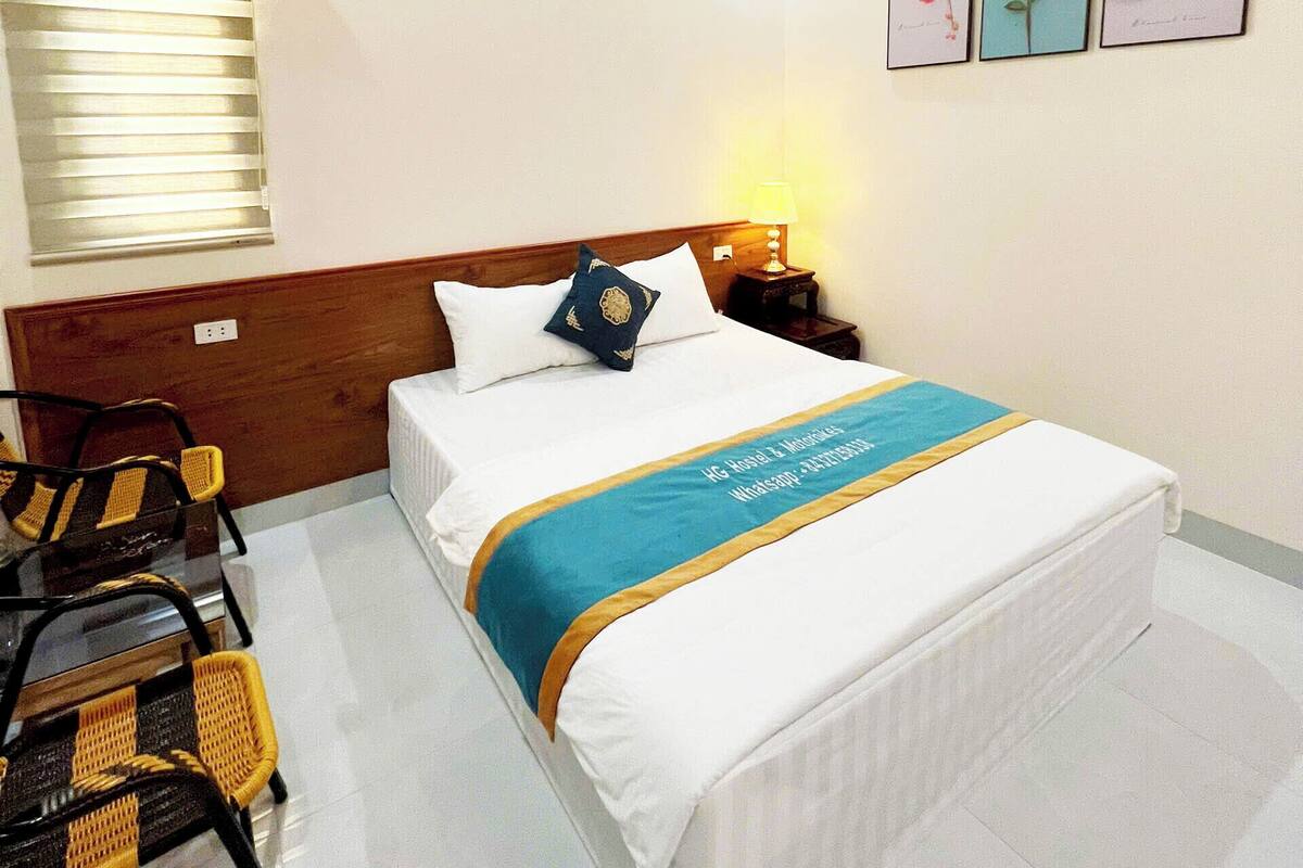 A hotel room with a bed, a nightstand, a lamp, a chair, and three framed pictures on the wall.