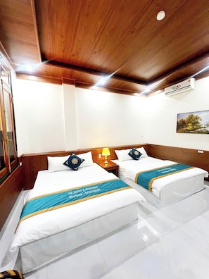Quarto de hotel com duas camas, cabeceiras de madeira, mesa de cabeceira com abajur, quadro na parede e unidade de ar condicionado.