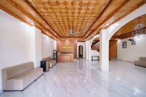 Um hall de hotel espaçoso com teto de madeira, balcão de recepção, sofá e lustre.