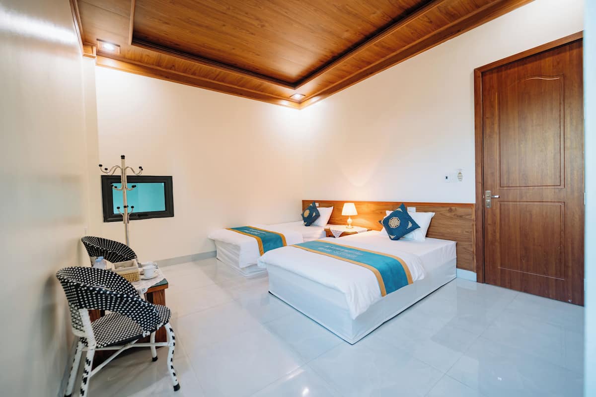 A hotel room with two beds, a wooden ceiling, a wooden door, and a small table with a chair.