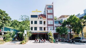 A multi-story building with a central entrance, surrounded by parked motorcycles and a few cars. - HG Hostel and Motobikes (Ha Giang 1)