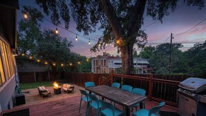 Una terraza con mesa y sillas, una parrilla y luces colgantes.