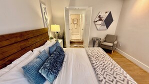Un dormitorio con una cama grande, un cabecero de madera, un sofá gris y una mesita de noche pequeña.