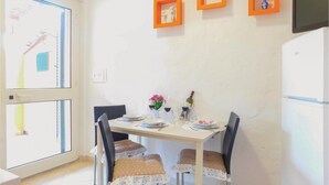 A dining area with a table set for four, chairs with heart-patterned cushions, a refrigerator, and a wall-mounted TV. - Amazing apartment in Gonnesa (Gonnesa)