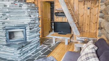 A cozy cabin interior with a stone fireplace, a television on a wooden table, and a couch with a plaid pillow.