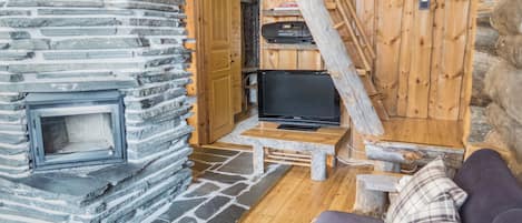 A cozy cabin interior with a stone fireplace, a television on a wooden table, and a couch with a plaid pillow.
