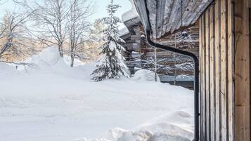 A snowy landscape with a wooden cabin and a snow-covered tree.