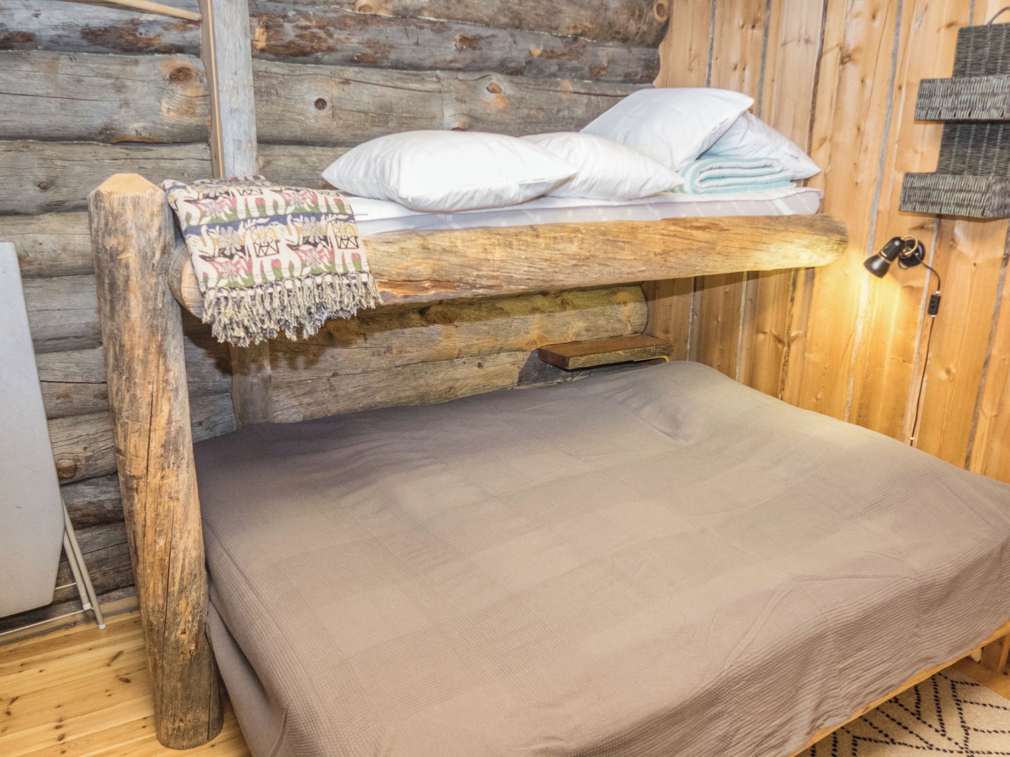 A bunk bed with a blanket and pillows, a wooden wall, and a small table with a lamp.