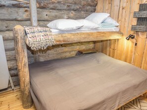 A bunk bed with a blanket and pillows, a wooden wall, and a small table with a lamp.