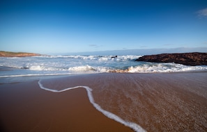 Une plage avec des vagues, un promontoire rocheux et un ciel dégagé.