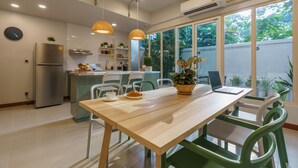 A modern kitchen with a dining area, featuring a wooden table, green chairs, and pendant lights.
