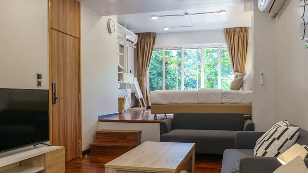 A modern living room with a sofa, a coffee table, a TV, and a bed with curtains.