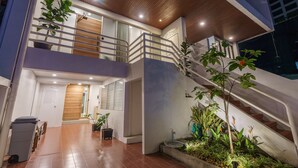 A modern two-story building with a staircase, potted plants, and a trash bin.