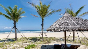 A beach scene with a thatched-roof hut, palm trees, and a sandy beach.
