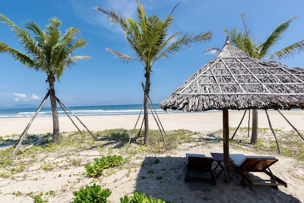 A beach scene with a thatched-roof hut, palm trees, and a sandy beach.