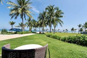 A grassy area with a wicker chair, palm trees, and a view of the ocean.