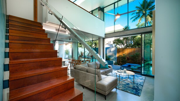 A modern interior with a wooden staircase, a beige sofa, and a glass coffee table.