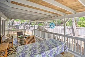 Un patio couvert avec une table et des chaises, un foyer en pierre et une vue sur une clôture en bois et des arbres.
