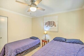 Une chambre avec deux lits, un ventilateur de plafond, une lampe fixée au mur et un tableau représentant un ours.