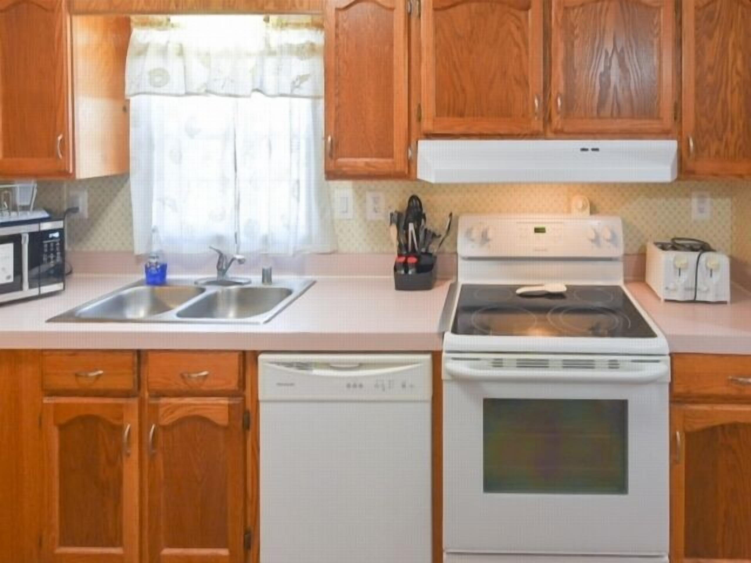 Una cocina con alacenas de madera, estufa blanca, lavavajillas y microondas.