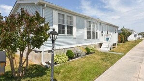 A single-story mobile home with a front porch, a small front yard, and a street lamp. - 3 BR 2 Bath Home featuring spacious deck 2 living areas 2 Community pools (Ocean City)