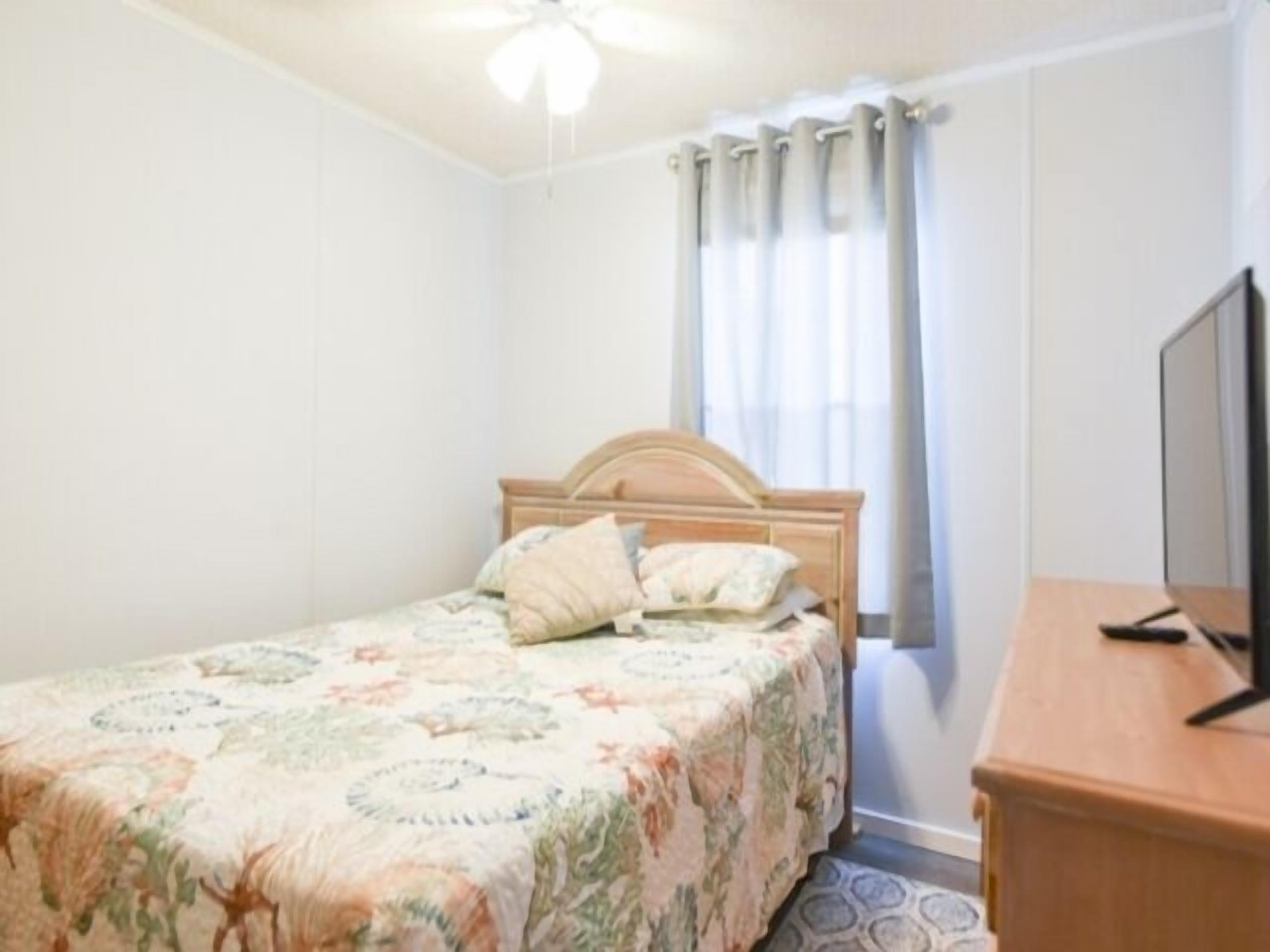 A bedroom with a bed, a wooden headboard, a television, and a window with curtains.