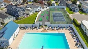 A residential area with a swimming pool surrounded by lounge chairs and umbrellas, a tennis court, and houses. - 3 BR 2 Bath Home featuring spacious deck 2 living areas 2 Community pools (Ocean City)
