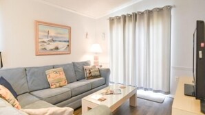 A living room with a sofa, a coffee table, a lamp, and a television. - 3 BR 2 Bath Home featuring spacious deck 2 living areas 2 Community pools (Ocean City)
