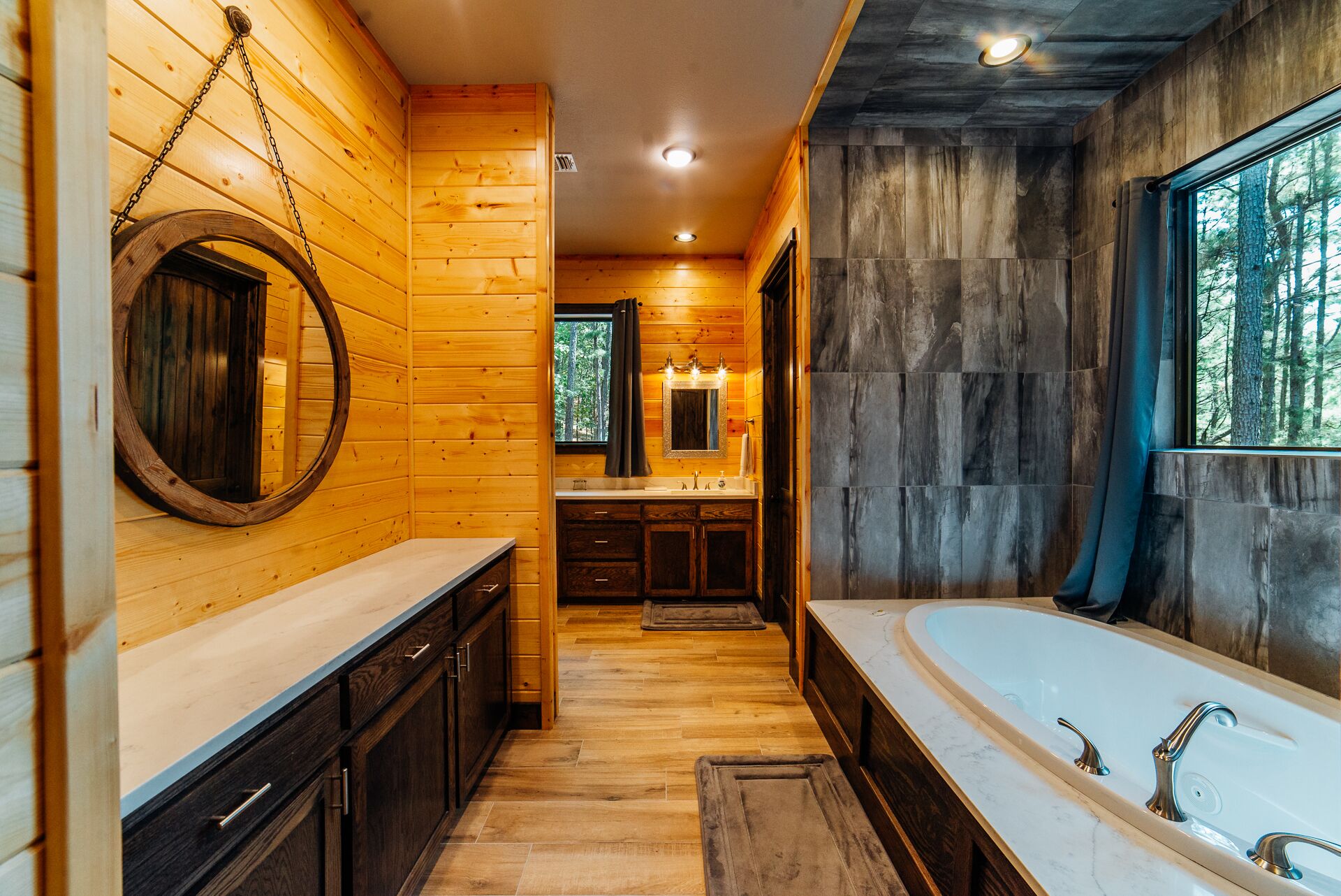 A modern bathroom with a wooden interior, a large bathtub, and a view of the forest.