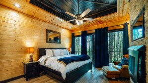 Une chambre confortable avec un plafond en bois, un lit avec une literie blanche, une table de chevet, un miroir, une fenêtre avec des rideaux et une cheminée.