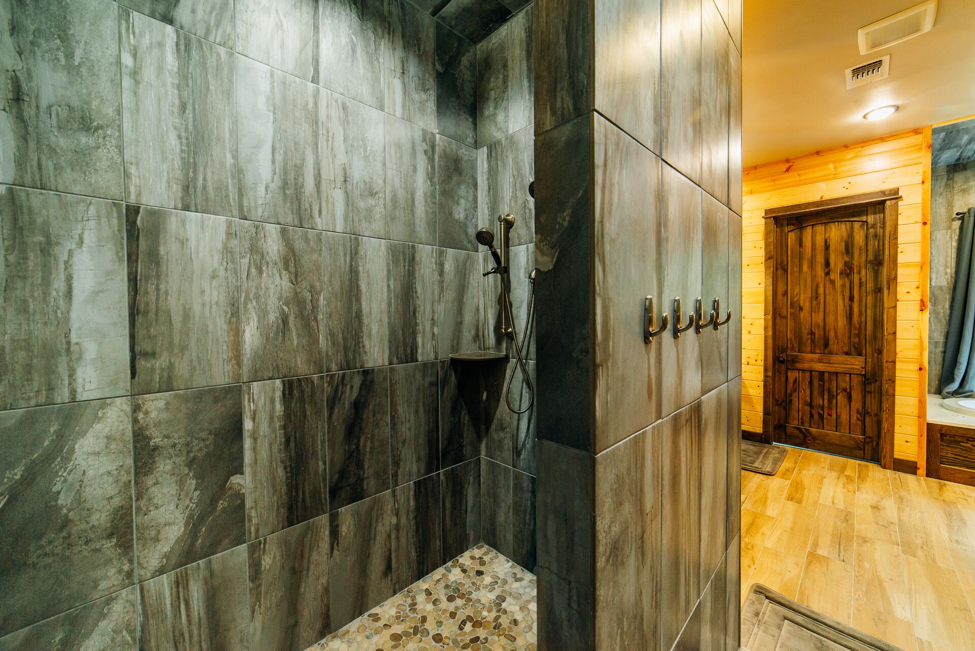 A modern bathroom with dark stone tiles, a shower area, and wooden paneling.