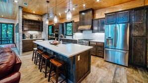 Une cuisine spacieuse dotée d’un grand îlot central, de meubles en bois foncé, d’appareils électroménagers en acier inoxydable et d’un plafond en bois.