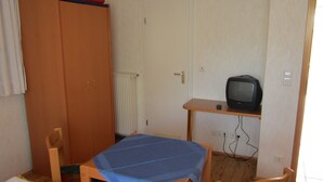 Ein Zimmer mit einem Holzschrank, einem kleinen Tisch mit blauer Tischdecke, einem Fernseher auf einem Schrank und einem Stuhl.