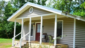 Eine kleine, einstöckige Hütte mit Veranda, einer roten Tür und einem Tisch mit Stühlen.