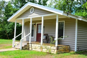 A small, single-story cabin with a porch, a red door, and a small table and chair set.