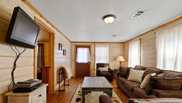 Ein gemütliches Zimmer mit Fernseher, Holzwänden, einer Couch, einem Couchtisch und einem Kamin.