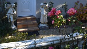 A house with a white door, a small porch, and a garden with statues and flowers.