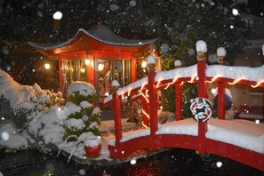 Un pont cobert de neu amb una estructura vermella tradicional i un arbre ple de neu al primer terme.